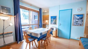 A cozy room with a dining table, chairs, a TV, a clock, and a bed. - 130m from ski slopes, 4th floor, balcony, parking, tv, ski locker, 35m², La Norma (La Norma)