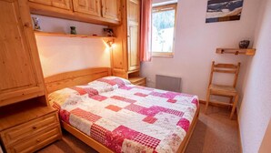 Ein Schlafzimmer mit einem hölzernen Bett, einem Nachttisch, einem Sessel und einem Fenster mit Bergblick.