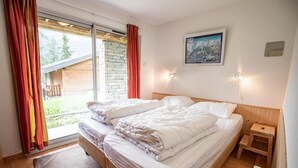 A double bed with white linens, a wooden headboard, a small bedside table, and a window with curtains.