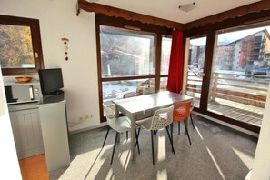 Una cocina compacta con microondas, una televisión pequeña y un comedor con mesa y sillas.