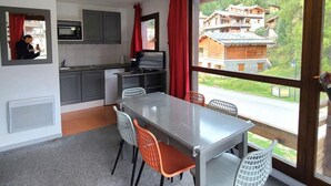 A modern kitchen with grey cabinets, a microwave, and a dining area with a grey table and orange chairs. - 300m from ski slopes, 1st floor, balcony, parking, tv, ski locker, 35m², La Norma (Villarodin-Bourget)