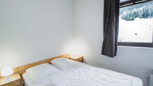 A simple, clean room with a bed, bedside table, and a window with a view of a snowy landscape. - 130m from ski slopes, 5th floor, balcony, parking, tv, ski locker, 35m², La Norma (La Norma)