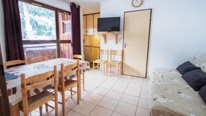 A room with a dining table, chairs, a sofa, a TV, and a door. - 130m from ski slopes, 5th floor, balcony, parking, tv, ski locker, 35m², La Norma (La Norma)