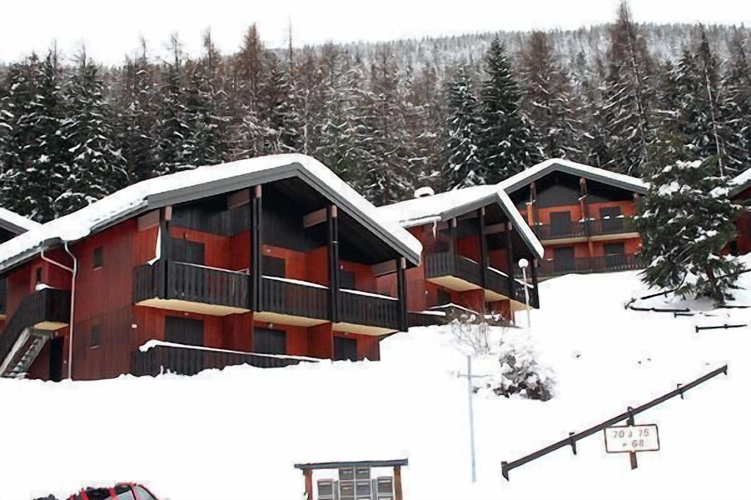 Een rij houten hutten met balkons, omringd door met sneeuw bedekte bomen.