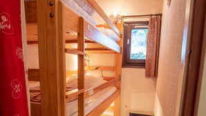 A narrow hallway with wooden bunk beds, a window with curtains, and a ventilation unit.