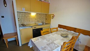 A compact kitchen with a tiled backsplash, a sink, and a stove. There is a dining table with chairs and a bench.