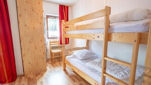 A bunk bed room with a wooden floor, a chair, and a window with red curtains.