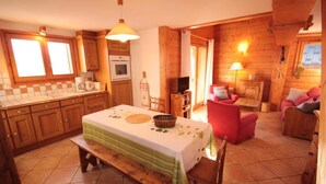 Een knus kamer in chaletstijl met een houten inrichting, een eettafel met een groene tafelkleed, een rode stoel en een open haard.
