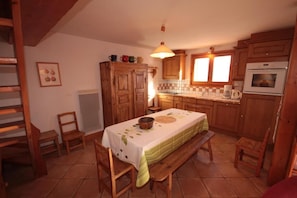 A cozy kitchen with wooden cabinets, a dining table with a green tablecloth, and a hanging light fixture.