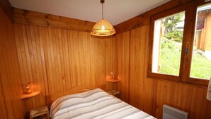 Ett sovrum med träpanel på väggarna, en säng, sänglampor, ett fönster och ett element.