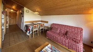 Una habitación acogedora con techo de madera, un sofá rojo con estampado, una mesa de comedor de madera con sillas y una mesita con revistas.
