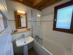 Une salle de bain avec un lavabo blanc, une cabine de douche en verre et une fenêtre à cadre en bois.