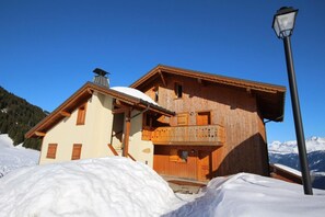 Una cabaña de madera con balcón, con una imponente montaña nevada al fondo.