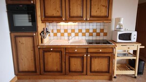 A kitchen with wooden cabinets, a tiled backsplash, a sink, a stove, and a microwave. - 200m from shops, 1st floor, swimming pool, balcony, tv, 46m², Les Saisies (Villard-sur-Doron)