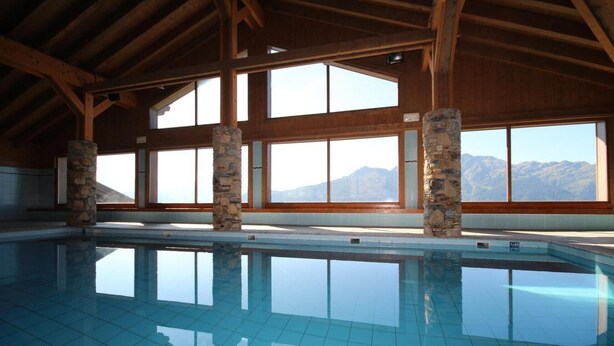 A large indoor swimming pool with stone pillars, large windows, and a view of mountains. - 200m from shops, 1st floor, swimming pool, balcony, tv, 46m², Les Saisies (Villard-sur-Doron)