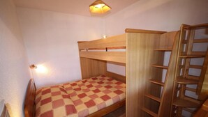 Un letto a castello con copriletto a quadretti, una scala in legno e una piccola unità a scaffali.