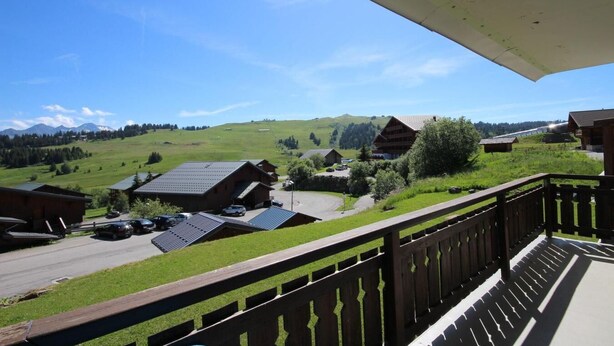 Vista da un balcone su una zona rurale con edifici in legno, cielo sereno e paesaggio collinare.