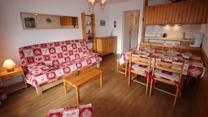 Ett mysigt vardagsrum med en mönstrad soffa, ett träbord som används som soffbord och en matplats med ett bord dukat för fyra personer.
