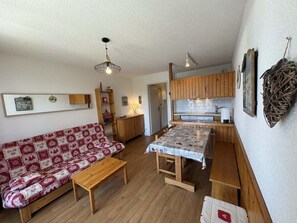 A compact living space with a sofa, a dining table, wooden cabinets, and a kitchenette.
