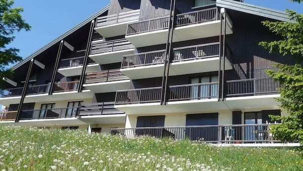 En byggnad med flera våningar, balkonger, ett platt tak och en trädgårdsdel med vita blommor.