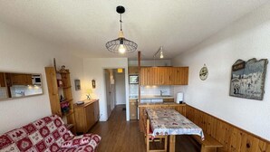 Ett mysigt rum med en träbänk, en soffa och ett bord med ett bordsskydd. Längst bak finns ett köksområde med träskåp och en hängande lampa.