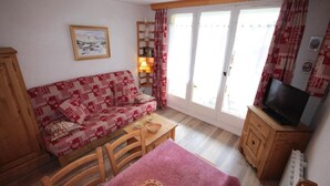A cozy living room with a patterned sofa, a wooden coffee table, a television on a wooden cabinet, and a sliding glass door with curtains. - 300m from ski slopes, Ground floor, view mountain, balcony, tv, 28m², Les Saisies (Les Saisies)