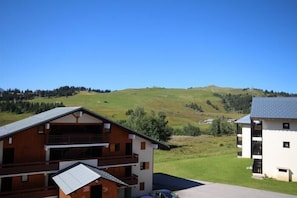 A two-story building with a balcony on the upper floor, surrounded by a green landscape and a clear blue sky. - 100m from ski slopes, 2nd floor, view ski slopes, balcony, parking, tv, ski locker, 25m² (Hauteluce)