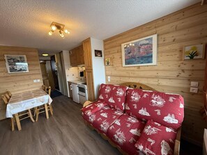 A cozy cabin interior with a dining table, a red sofa, wooden walls, and a kitchen area.