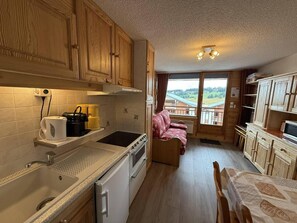 A compact kitchen with wooden cabinets, a sink, a stove, and a dining area with a table and chairs. - 100m from ski slopes, 2nd floor, view ski slopes, balcony, parking, tv, ski locker, 25m² (Hauteluce)