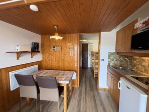A compact kitchen with wooden cabinets, a dining table with chairs, a built-in oven, and a microwave.