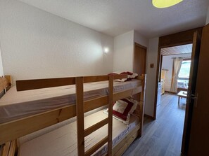 A bunk bed room with a wooden headboard, a door leading to a balcony, and a view of the outside.