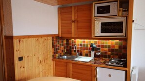 A compact kitchen with wooden cabinets, a microwave, a stove, and a sink. - 100m from ski slopes, 1st floor, view ski slopes, balcony, tv, ski locker, 23m², Les Saisies (Les Saisies)