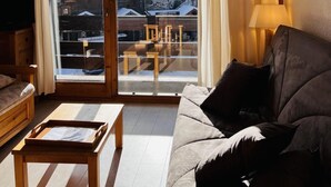 A cozy living room with a sliding glass door leading to a balcony, a sofa, a small wooden table, and a lamp. - 100m from ski slopes, 1st floor, view ski slopes, balcony, tv, ski locker, 23m², Les Saisies (Les Saisies)