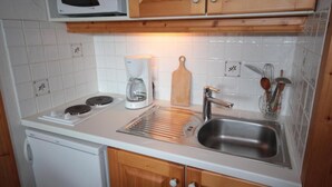 Een compacte keuken met een magnetron, koffiezetapparaat, spoelbak en houten kastjes.