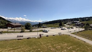 A parking lot with vehicles, a building with a sloped roof, and a mountainous backdrop. - 200m from ski slopes, 1st floor, view ski slopes, balcony, tv, ski locker, 24m², Les Saisies (Les Saisies)