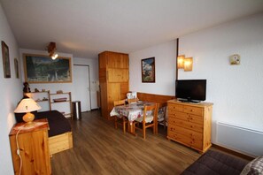 A compact living space with a dining area, a television, wooden furniture, and a painting on the wall.