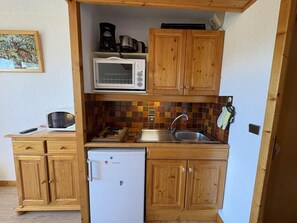 A compact kitchen with wooden cabinets, a microwave, a coffee maker, and a refrigerator.