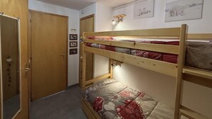 Une chambre avec des lits superposés, une porte en bois, un luminaire et des tableaux encadrés accrochés au mur.