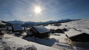 Un village enneigé, avec ses maisons traditionnelles en bois, un ciel dégagé et une chaîne de montagnes en toile de fond.