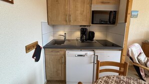 Eine kompakte Küche mit Holzausstattung, einer Mikrowelle, einer Kaffeemaschine und einem Geschirrspüler.
