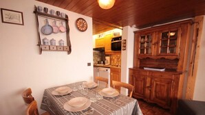 A dining area with a table set for four, wooden cabinets, and a kitchen in the background. - 100m from ski slopes, 1st floor, view ski slopes, balcony, tv, ski locker, 26m², Les Saisies (Les Saisies)
