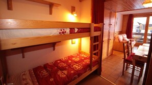 Un lit superposé avec une couvre-lit à motifs rouges, une tête de lit en bois et une petite table avec une chaise.