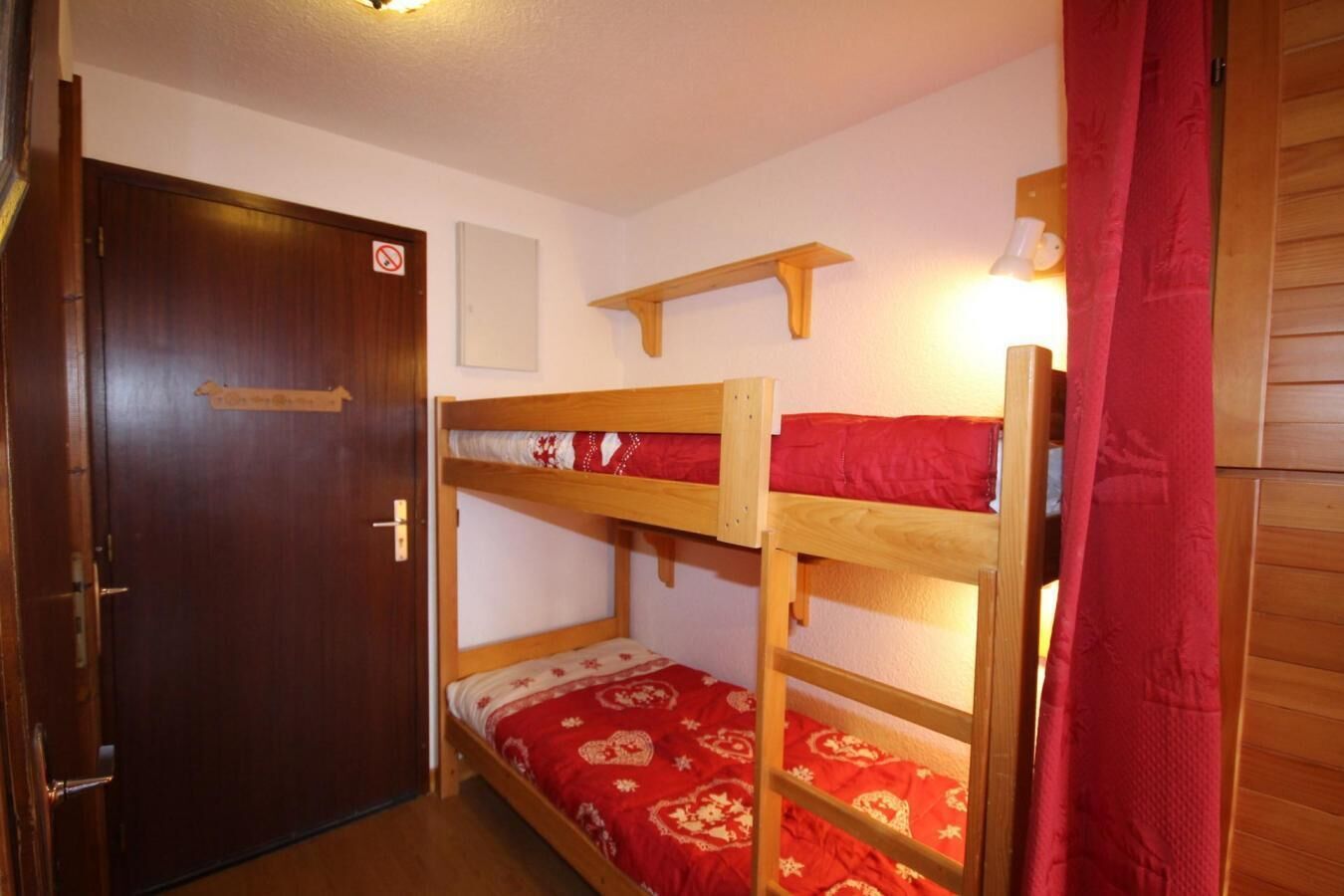 A bunk bed room with a wooden door, a small shelf, and a red curtain.