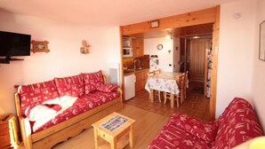 Una sala de estar acogedora con un sofá rojo estampado, una mesita de madera con una revista, y una zona de cocina con microondas y fregadero.
