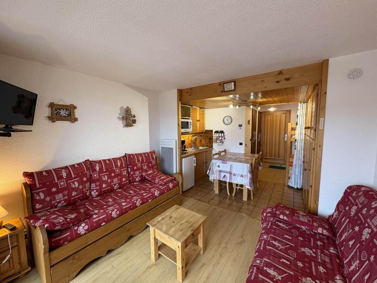 A cozy living room with a red patterned sofa, a wooden coffee table, and a dining area with a table and chairs.