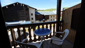 Un balcón con una mesa redonda y dos sillas, con vistas a una zona rural con edificios y cielo despejado.