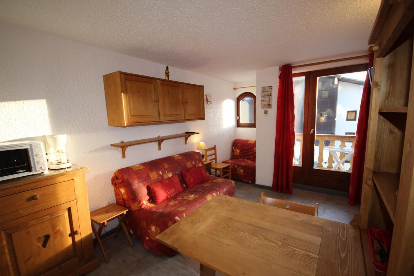 A cozy room with a wooden sofa, a dining table, a microwave, and a cabinet.