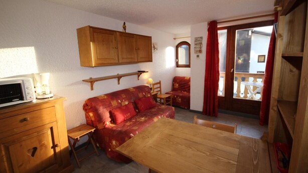Una habitación acogedora con un sofá de madera, una mesa de comedor, un microondas y un armario.