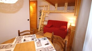 Ein gemütlicher Raum mit einem Schlafplatz in einer Holzbalkonage, einem roten Sofa und einem Esstisch mit Zeitschriften.