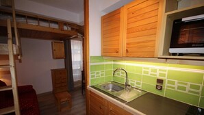 Eine kompakte Küche mit Holzausstattung, einer grunen Fliesenrückwand und einer eingebauten Mikrowelle.